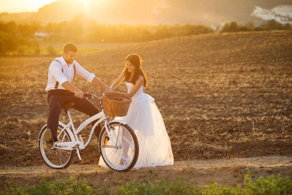 novio en bicicleta con novia de pie en sembrado